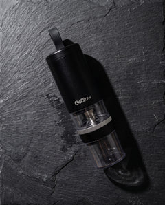 GoBlow Precision Device flat lay on dark slate — machined stainless EDC capsule pendant